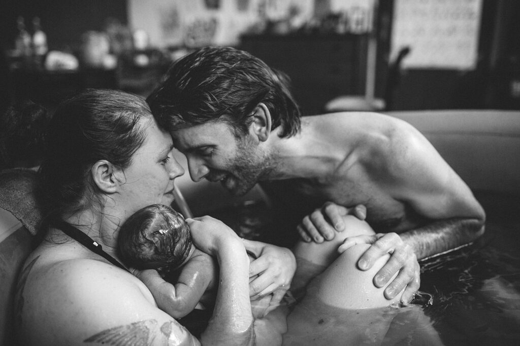Geburtsfotografie begleitend während Hausgeburt im Geburtspool und stolzer Vater