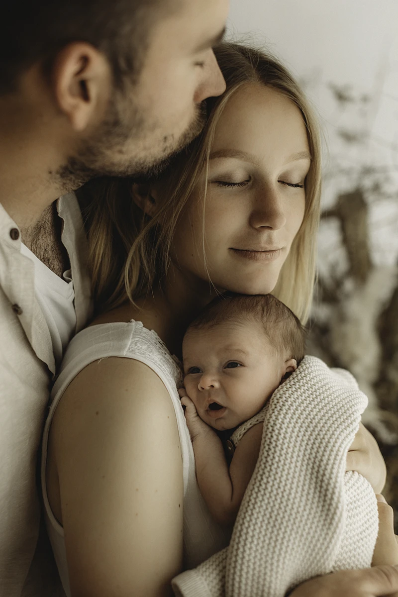 Mutter und Vater umarmend ihr Neugeborenens Baby beim Newborn Fotoshooting ganz kuschlig und warm herzlich innig